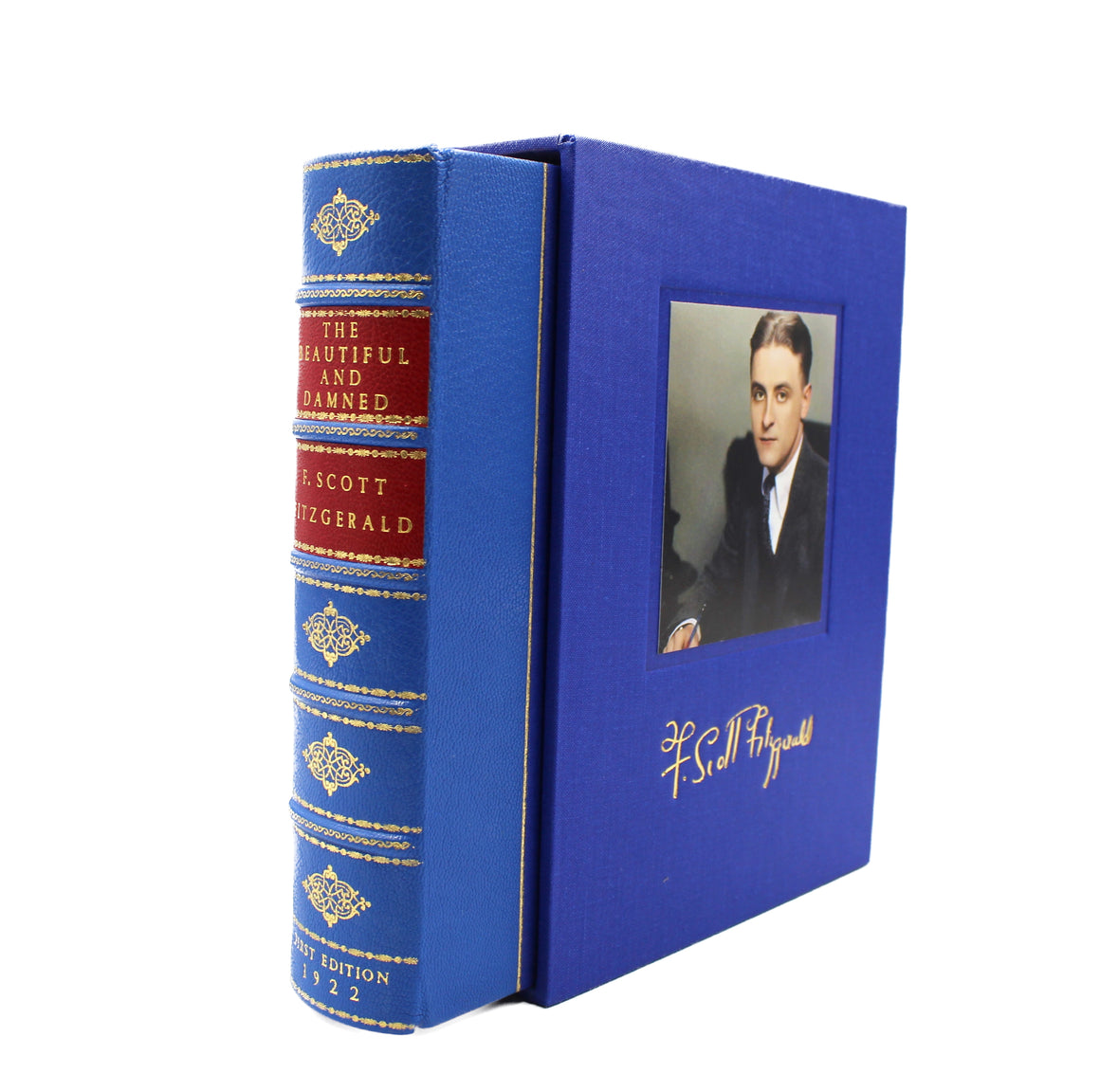 The novel and it's clamshell, with the novel angled so that the spine is visible. The slipcase is facing forward, showing off Fitzgerald's facsimile signature in gold ink under an inset portrait. The spine of the Novel is blue and red with gold gilding.