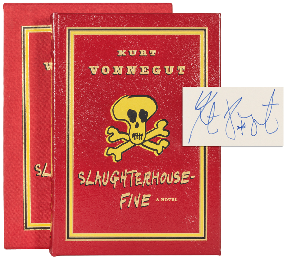 The novel and its slipcase, with the novel angled so that the spine is visible. The novel and the slipcase are identical in cover art. The spine of the novel features the same yellow, black and gold scheme. At the top and bottom of the novel's spine is a pair of illustrated eyes, and in the center "Slaughter-House-Five" written out vertically in a strip of yellow leather. 